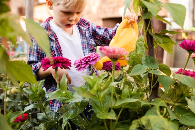 The toddler is watering flowers in the garden using a watering can