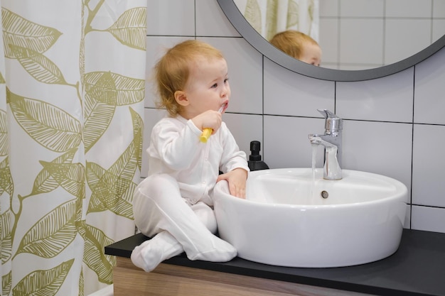 A toddler sitting on the washbasin cabinet and brushing teeth Daily morning hygiene routine