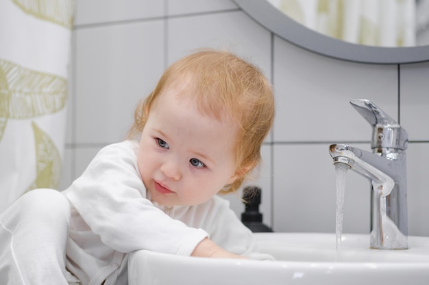 Toddler washing hands in sink sitting on washbasin cabinet Daily morning hygiene routine