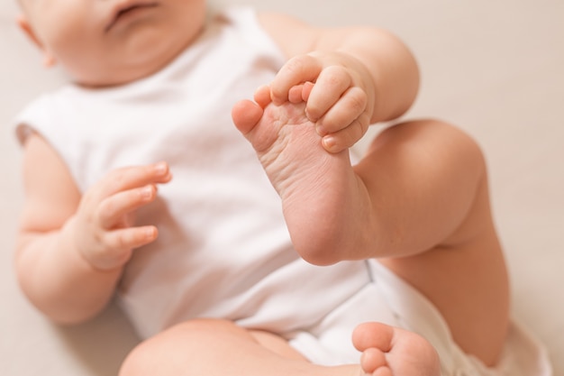 Toddler in white bodysuit 5 months lies on the wooden floor of the house view from above