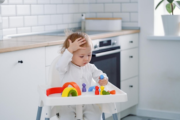 A toddler with a hand on his head in highchair playing with rainbow toy Early child development