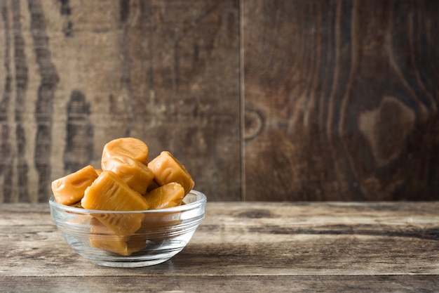 Toffee caramel candies in a crystal bowl on wooden table copy space