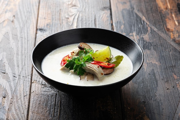 Tom kha gai thai galangal coconut soup in a black bowl on a wooden background selective focus