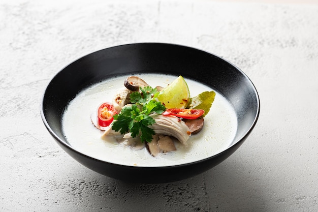 Tom kha gai thai soup in a black bowl on a concrete background selective focus