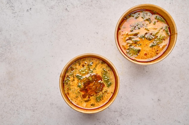 Tom yam soup with salmon and seafood in two paper solid containers on light background designer food