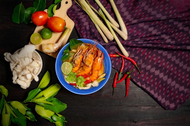 Tom Yum Goong Spicy Sour Soup on wooden table and Thai fabric, top view,