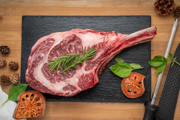 Tomahawk beef steak with rosemary on black plate Fresh Tomahawk beef on wooden background