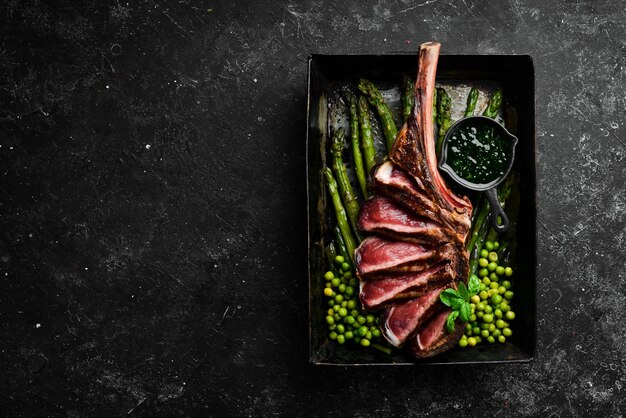 Tomahawk steak on the bone Grilled steak with asparagus and green peas On a black background Top view Free copy space