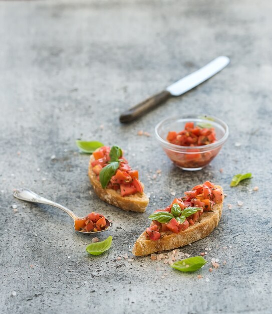 Photo tomato and basil bruschetta sandwich over grunge gray background.