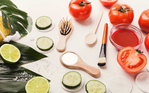 Tomato face mask and cucumber eyes patches for natural beauty care. Jar of juicy paste, red fresh vegetable, applicator brush on white background, homemade cosmetic and spa concept, copy space