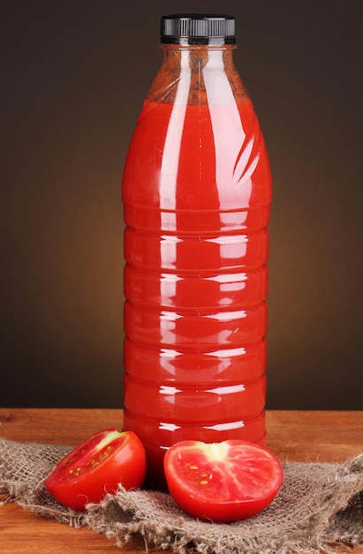 Tomato juice in bottle on wooden table on brown background