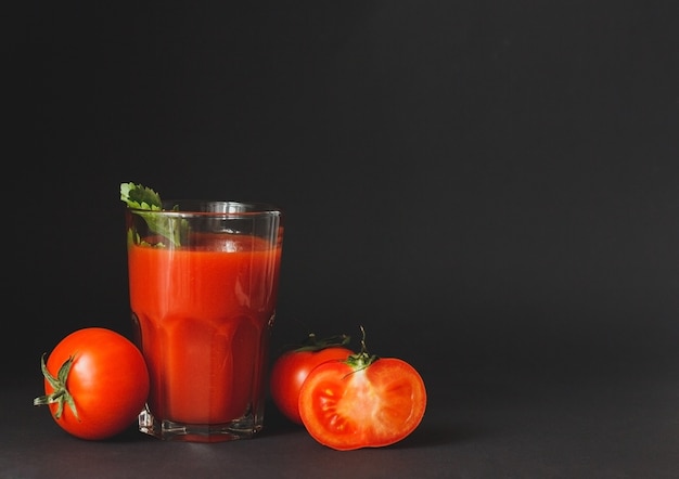 Tomato juice in a glass with fresh tomatoes on black background