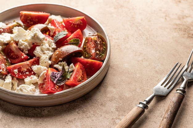 Tomato salad with feta cheese and herbs served with cutlery on beige background with text space