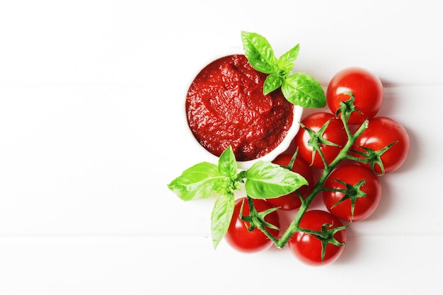 Tomato sauce in a small white gravy boat with ingredients for the sauce on a white wooden background