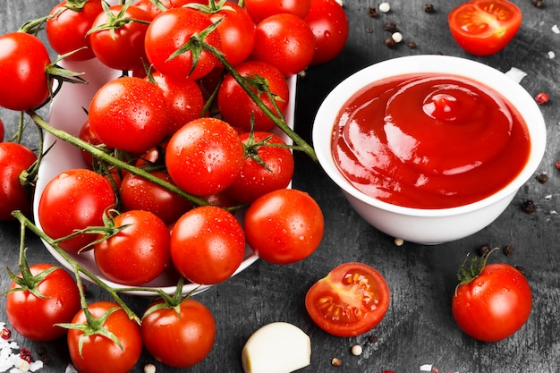 Tomato sauce in white bowl, spice and cherry tomatoes on a dark background