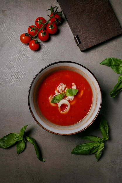 tomato soup with squid in a plate on a gray background, next to a wooden menu and tomatoes, top view