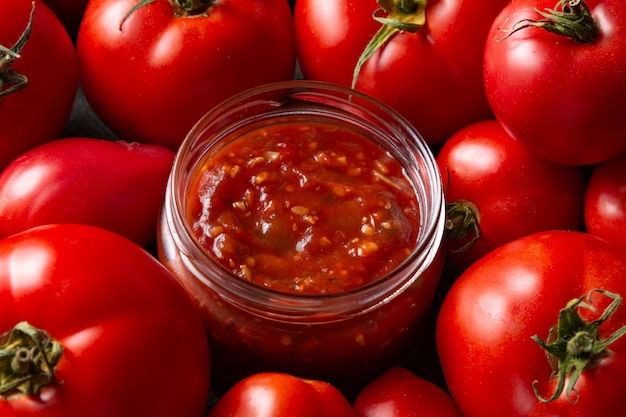 Tomato stew in a glass jar with tomatoes in the background on a wooden table