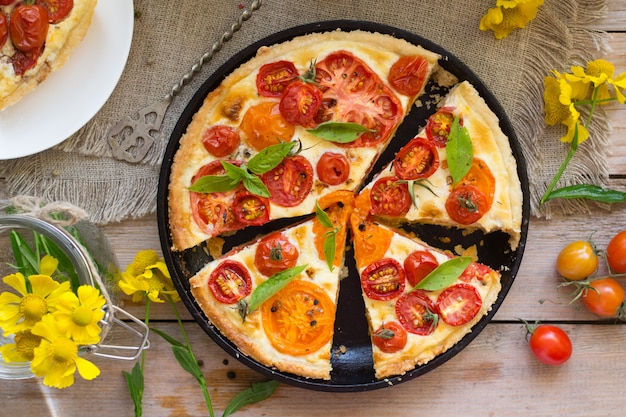 Tomato tart made with shortcrust  pastry, red and yellow tomatoes, cheese and cream. Concept of healthy eating or vegetarian food on rustic wooden background