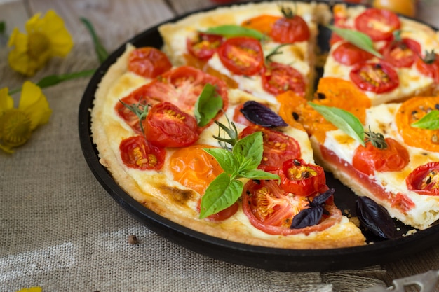 Tomato tart made with shortcrust  pastry, red and yellow tomatoes, cheese and cream. Concept of healthy eating or vegetarian food on rustic wooden background