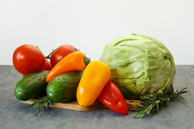 Tomatoes, cabbage, sweet peppers and cucumbers on grey table and white wall background