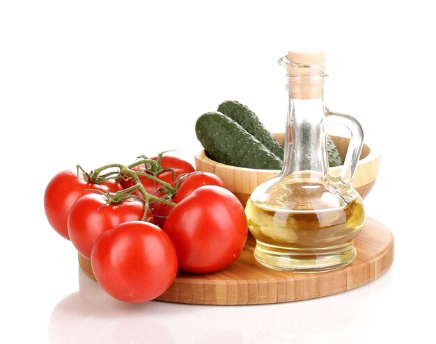 Tomatoes and cucumbers with oil on wooden board isolated on white