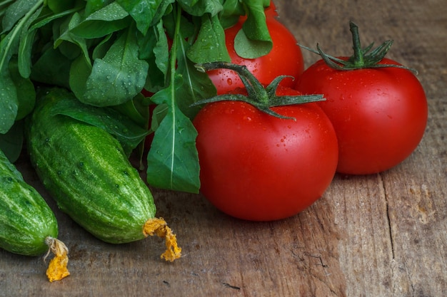 Tomatoes and cucumbers with salad on the background of wood