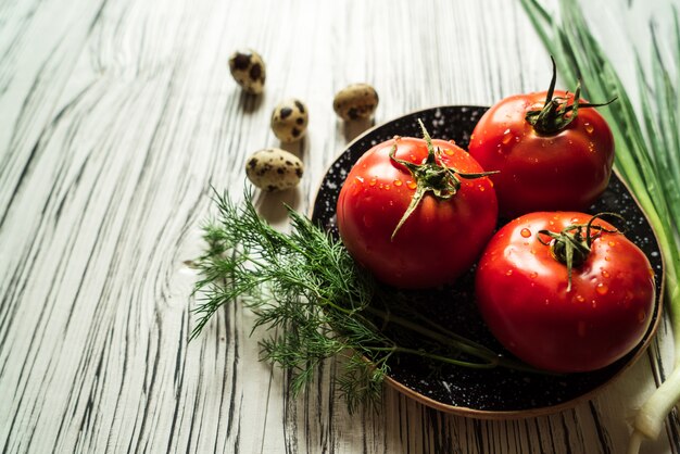 Tomatoes and greens on a white wooden table