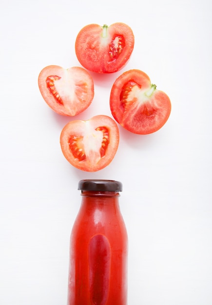 Tomatoes juice in bottle and fresh tomatoes slices on white wooden background