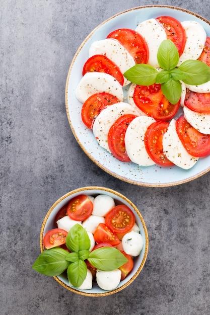 Tomatoes, mozzarella cheese, basil and spices on gray slate stone chalkboard. Italian traditional caprese salad ingredients. Mediterranean food.