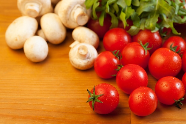 Tomatoes, mushrooms and arugula on wooden table, focus on foreground