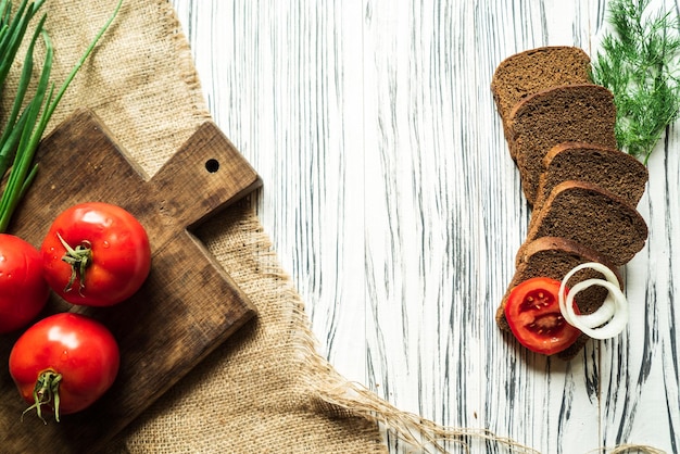 Tomatoes and onions greens and rye bread on a white wooden table