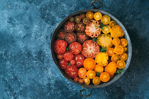 Tomatoes in slices of different colors in a pan on dark