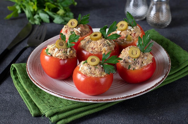 Tomatoes stuffed with tuna and olives on a round plate on a dark gray background