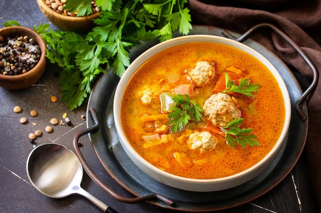 Tomatolentil soup with meatballs and vegetables on a dark slate table top