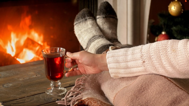 Toned closeup image of young woman holding cup of tea at burning fireplace in living room