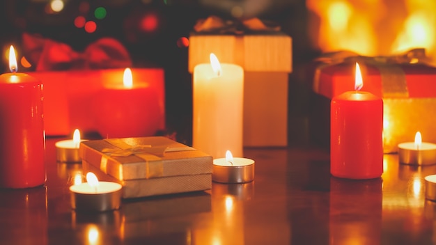 Toned image of burning candles, gifts and presents on wooden table on Christmas eve