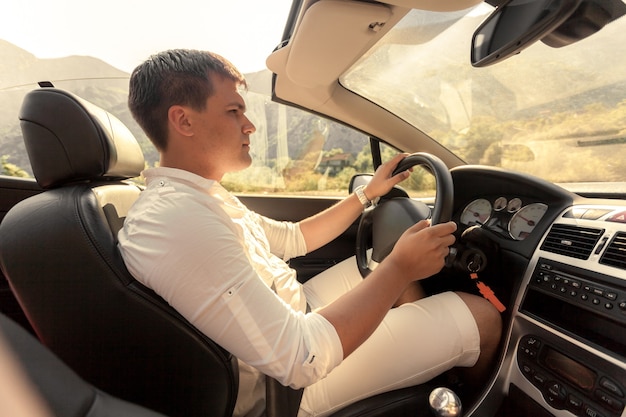 Toned photo of handsome young man driving convertible at sunny day