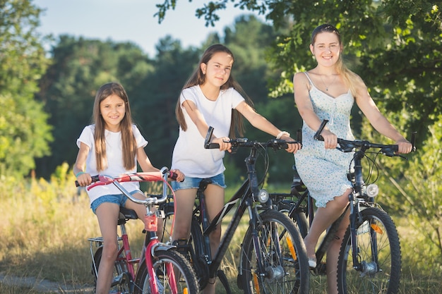 Toned portrait of two sister cycling with mother at meadow by the lake