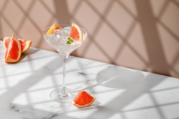 Tonic cocktail Fresh Cold drink with ice fresh grapefruit Beige marble background with window shadow