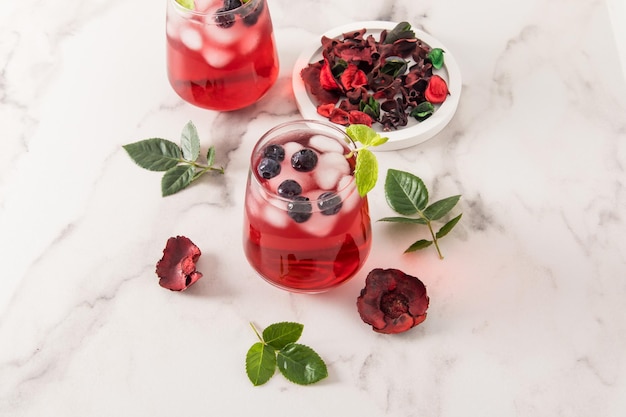 Tonic vitamin drink from rose petals hibiscus with blueberries mint leaves ice cubes in glasses on a marble table iced tea