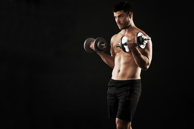 Toning and defining his physique Studio shot of a sporty young man working out with dumbbells isolated on black