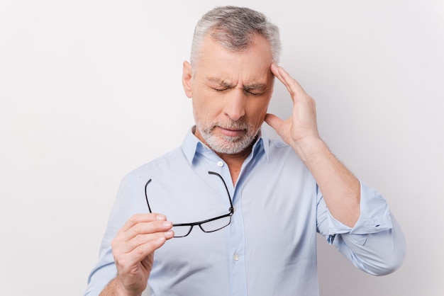 Too stressful day. Frustrated senior man in shirt touching head with fingers and keeping eyes closed while standing against white background