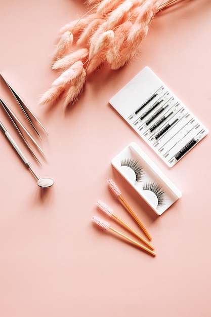 Tools for eyelash extension on trendy pastel pink background False eyelashes tweezers and brushes Beauty shop Makeup cosmetics Top view flat lay