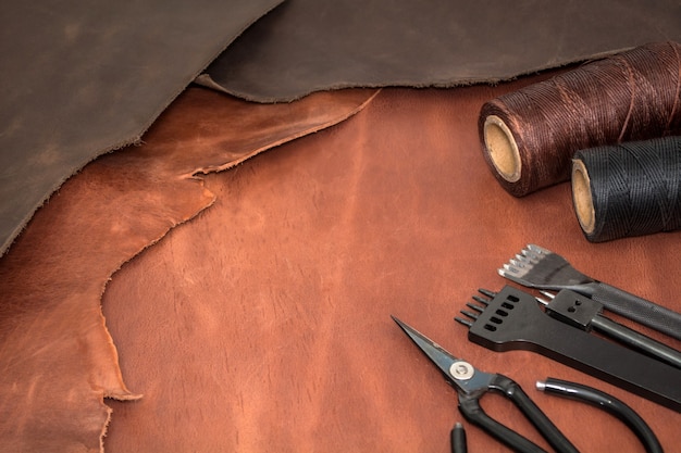 Tools for leather crafting and pieces of brown leather. Manufacture of leather goods. View from above flat lay. Empty space for text