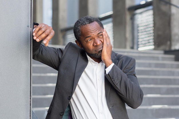 Toothache on the street a senior african american man in a suit stands outside an office and holds