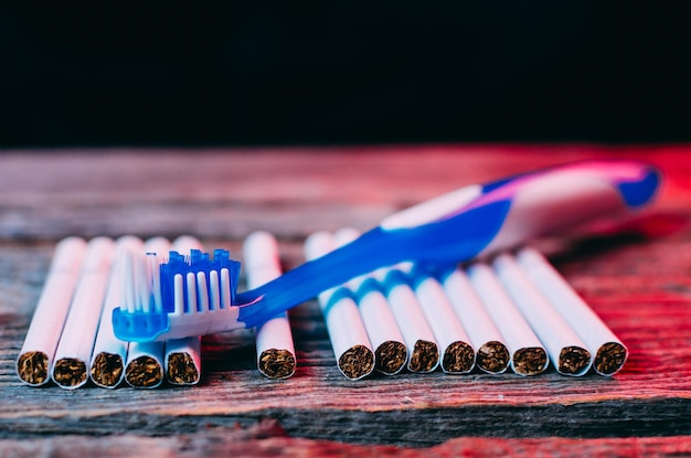 Toothbrush and cigarettes on wooden background with red backlight