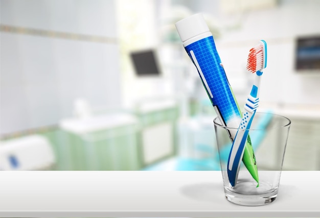 Toothbrush and toothpaste in glass on blurred background