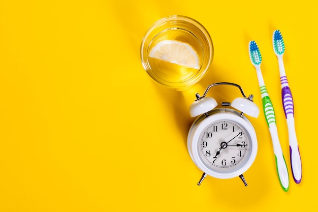 Toothbrushes, glass of water with lemon and alarm clock