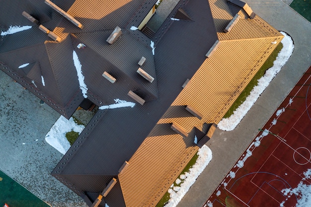 Top aerial view of building brown shingle tiled roof with complex configuration construction.