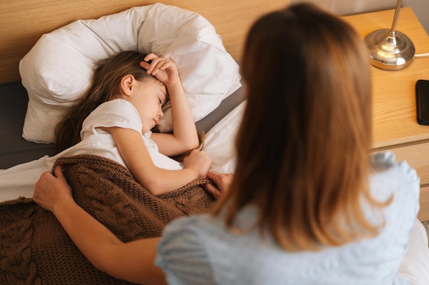 Top back view of adorable sick little girl sleeping on bed in children room under blanket at home